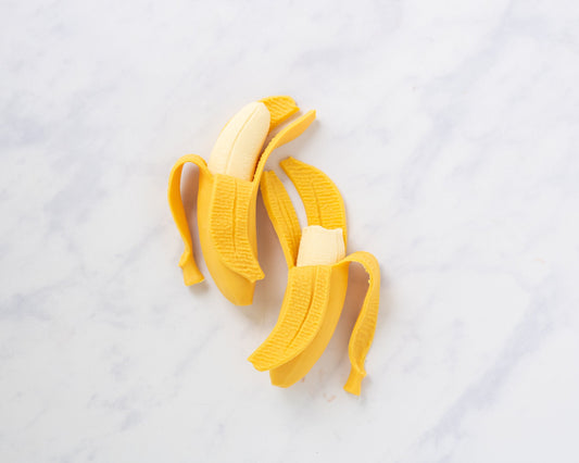 Two half-peeled banana squishy stress balls on white marble — Lil' Slimetastic