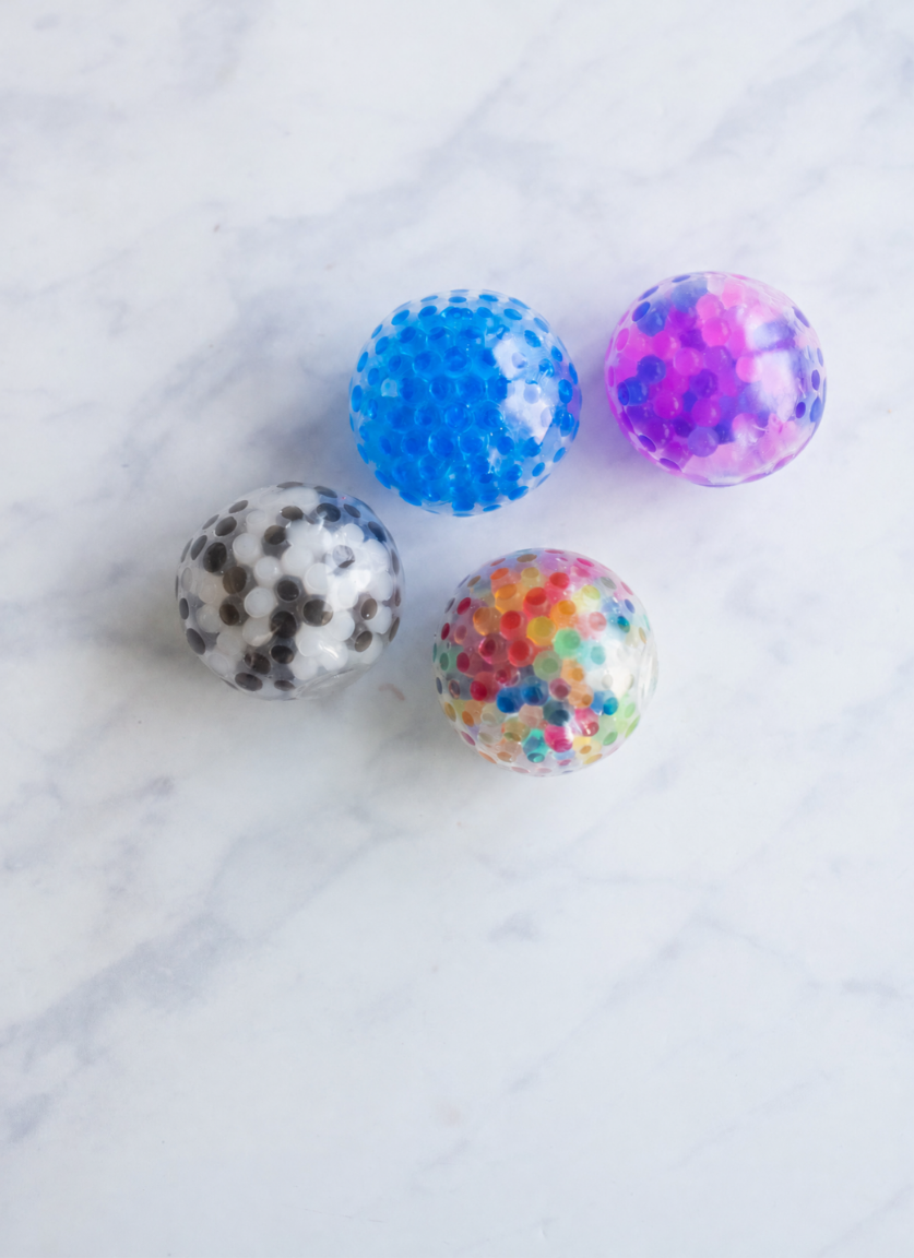 Four jelly bead stress balls in blue, purple and blue, black and white, and multi colour on a marble table