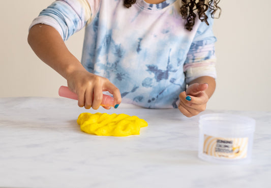 Child spraying slime activator spray onto yellow slime to fix stickiness