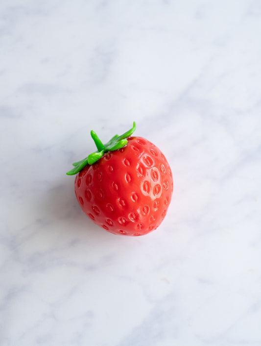 Red strawberry squishy stress ball with green stem on white marble — Lil' Slimetastic